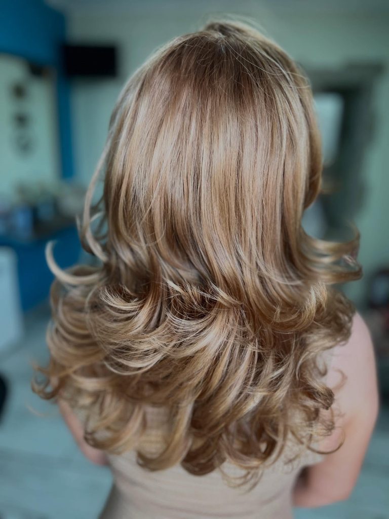 Păr lung, cu nuanțe blonde și bucle lejere, fotografiat în salon.